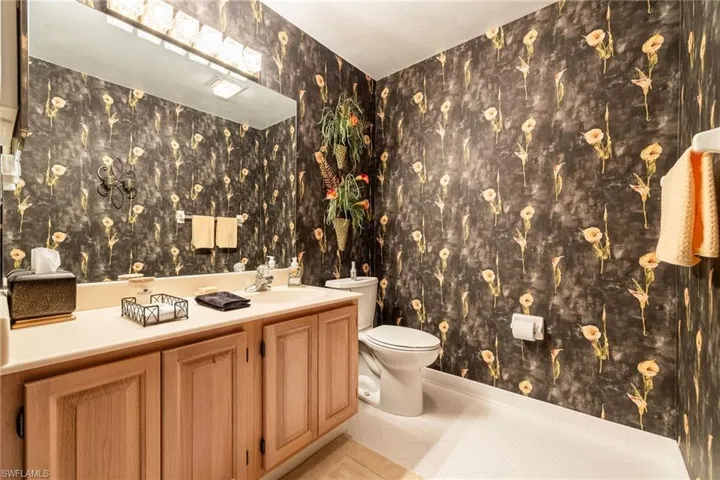 Downstairs guest half bath with wallpapered walls, vanity, and light tile patterned floors