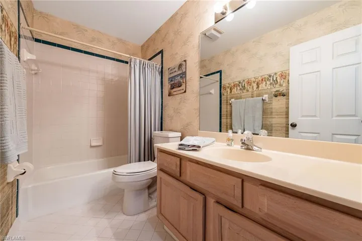Full bathroom featuring vanity, shower / tub combo, light tile patterned floors, and wallpapered walls