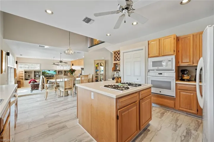 Kitchen featuring ceiling fan, light countertops, a center island, white appliances, and recessed lighting