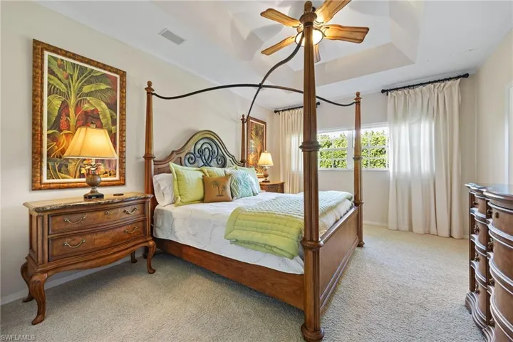 Primary bedroom with light colored carpet, a ceiling fan, ornamental molding, and a tray ceiling