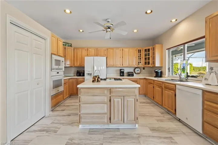 Kitchen featuring glass insert cabinets, light countertops, recessed lighting, white appliances, and a center island with sink