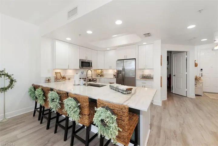 Kitchen featuring light stone counters, stainless steel appliances, a peninsula, white cabinets, and light wood-type flooring