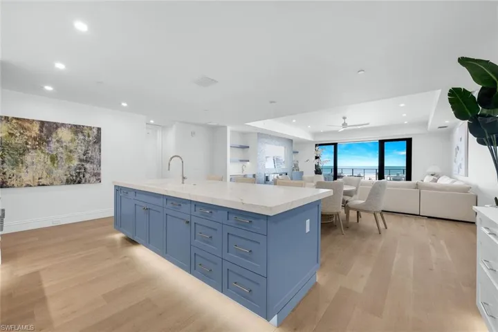 Kitchen with blue cabinetry, a kitchen island with sink, open floor plan, a tray ceiling, and light wood-type flooring