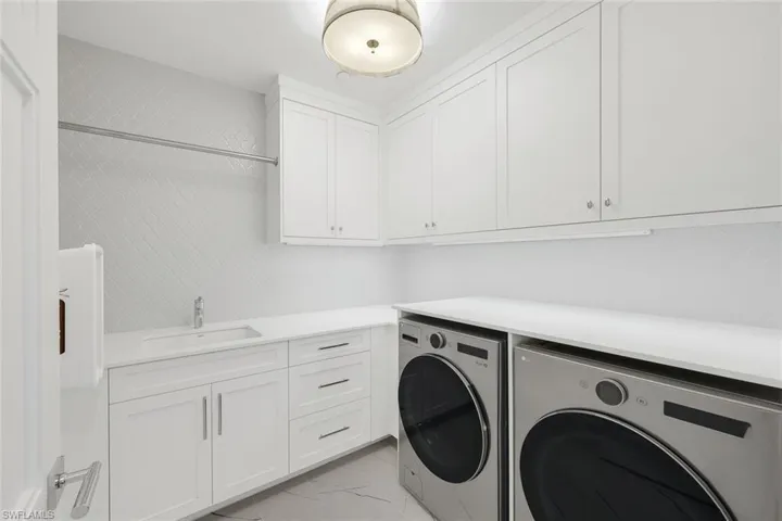 Laundry area featuring washing machine and dryer, cabinet space, and light marble finish floors