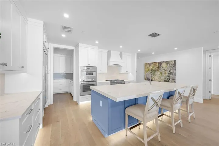 Kitchen with a large island, dual tone cabinets, light wood finished floors, double oven, and recessed lighting