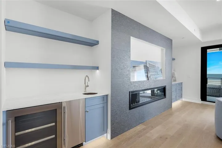 Indoor wet bar featuring open shelves, wine cooler, light stone counters, light wood finished floors, and stainless steel refrigerator