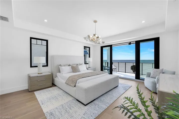 Bedroom with a water view, a raised ceiling, light wood-style flooring, access to exterior, and suspended lighting