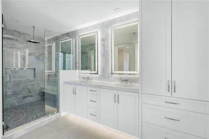 Full bathroom featuring double vanity, a marble finish shower, and light tile patterned floors