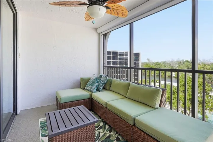 Screened in lanai with a ceiling fan, outdoor couch, coffee table, rug, table and chair set with a matching table under the TV.