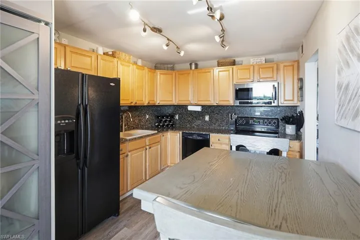 Kitchen with granite counters and backsplash, lighter cabinets, small dining table, black appliances, and a laundry closet.