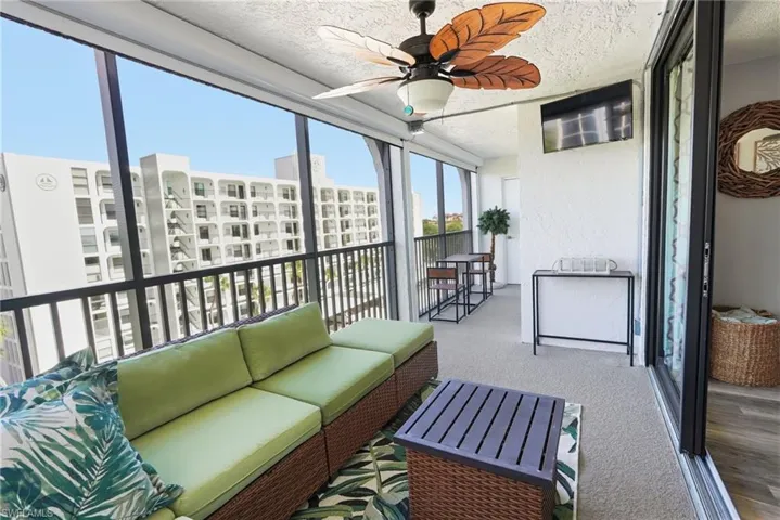 Screened in lanai with a ceiling fan, outdoor couch, coffee table, rug, table and chair set with a matching table under the TV.