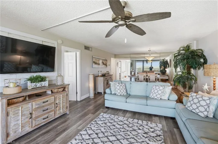 Living room with a ceiling fan, 2 couches, chair, 2 end tables, a TV stand and a wood wall behind the TV.