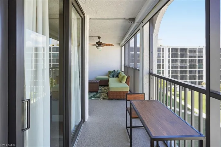 Screened in lanai with a ceiling fan, outdoor couch, coffee table, rug, table and chair set with a matching table under the TV.