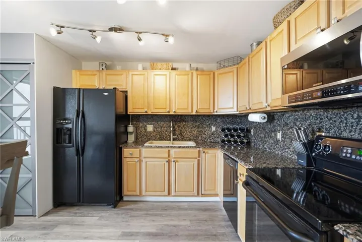 Kitchen with granite counters and backsplash, lighter cabinets, small dining table, black appliances, and a laundry closet.
