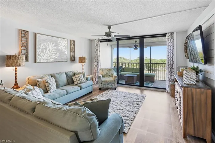 Living room with a ceiling fan, 2 couches, chair, 2 end tables, a TV stand and a wood wall behind the TV.