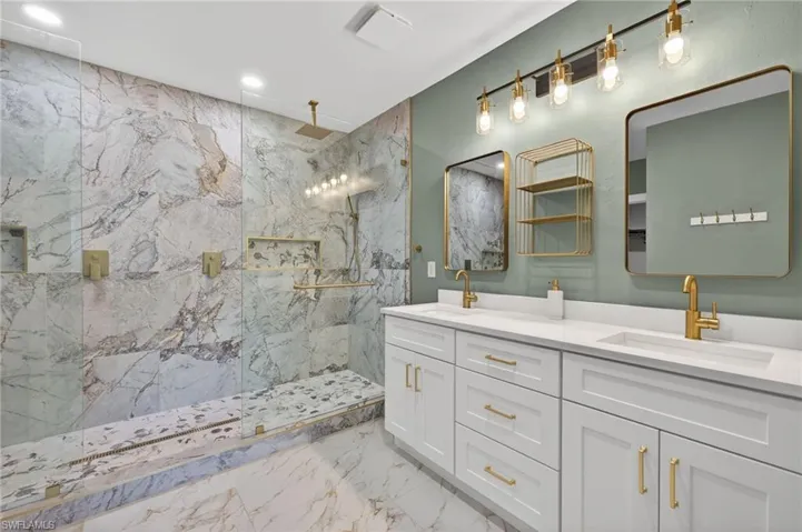 Bathroom featuring double vanity, a marble finish shower, recessed lighting, and light marble finish flooring