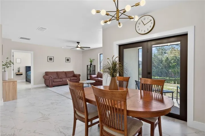 Dining room with healthy amount of natural light, light marble finish flooring, ceiling fan, and suspended lighting