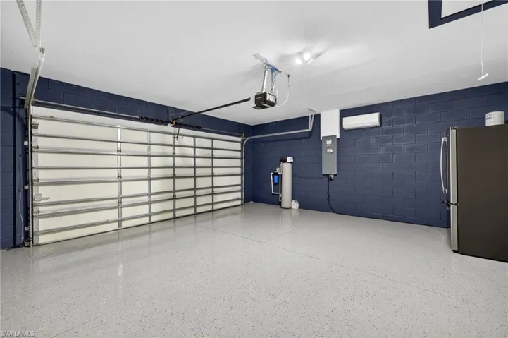 Garage with concrete block wall, freestanding refrigerator, electric panel, and a garage door opener