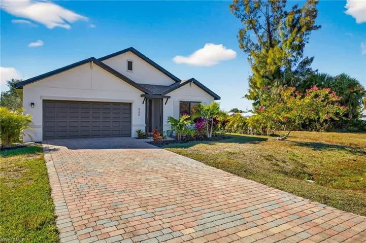 View of front of property with a front lawn, decorative driveway, stucco siding, and a garage