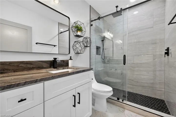 Full bath featuring a shower stall, vanity, and light marble finish floors