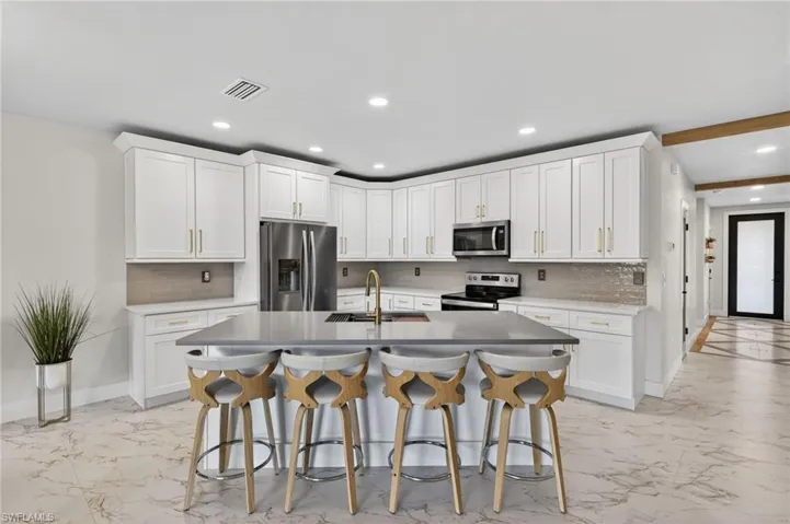 Kitchen with a breakfast bar, white cabinetry, stainless steel appliances, backsplash, and a center island with sink