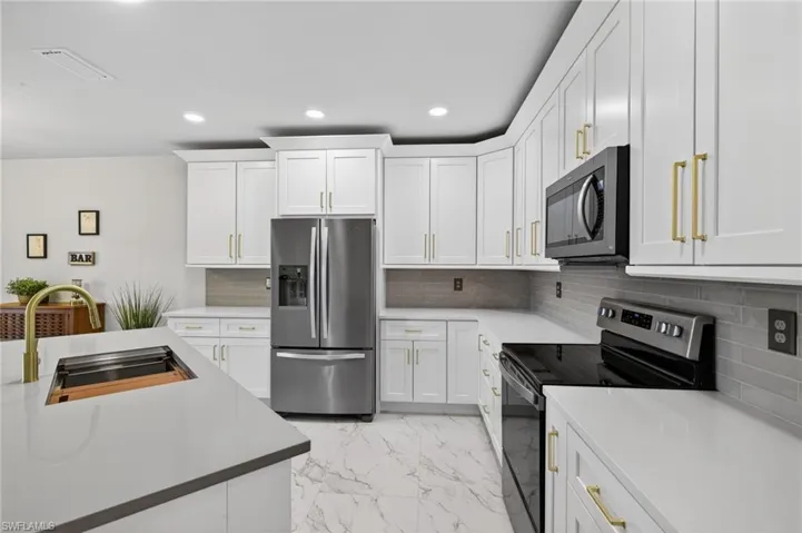 Kitchen featuring stainless steel appliances, light marble finish floors, white cabinets, and recessed lighting