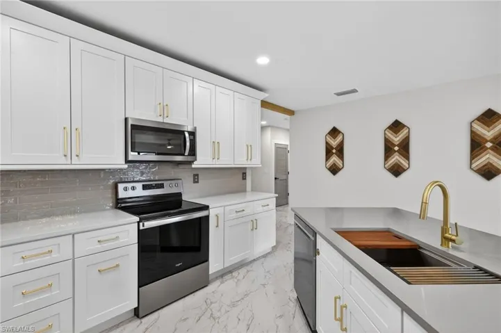 Kitchen with stainless steel appliances, white cabinets, light stone counters, light marble finish floors, and recessed lighting