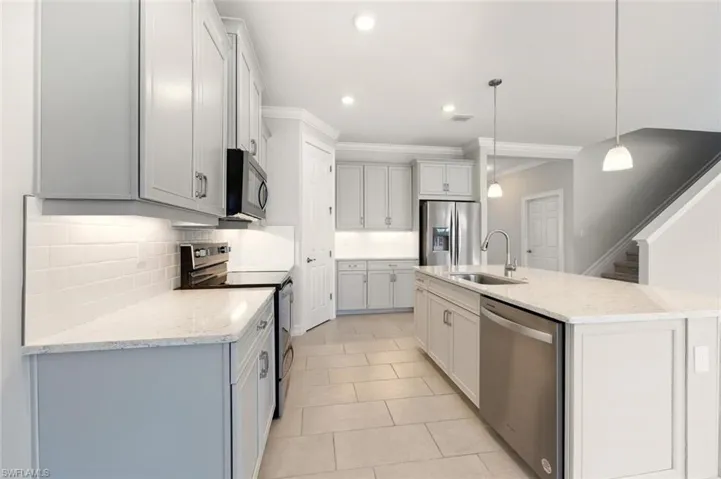 Kitchen with stainless steel appliances, decorative backsplash, light stone counters, a kitchen island with sink, and pendant lighting