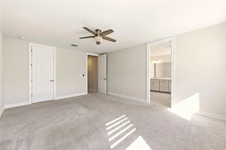 Unfurnished bedroom with a ceiling fan, light colored carpet, and ensuite bathroom
