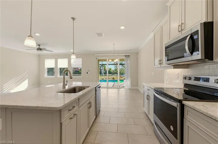 Kitchen with stainless steel appliances, light stone countertops, a center island with sink, suspended lighting, and white cabinets
