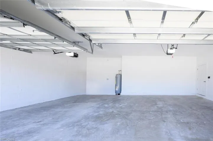 Garage with concrete block wall, water heater, and a garage door opener