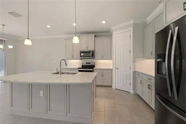 Kitchen with stainless steel appliances, ornamental molding, light stone countertops, a center island with sink, and backsplash