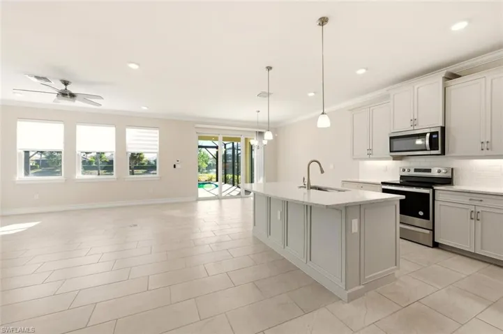 Kitchen with stainless steel appliances, backsplash, ornamental molding, light stone counters, and a center island with sink