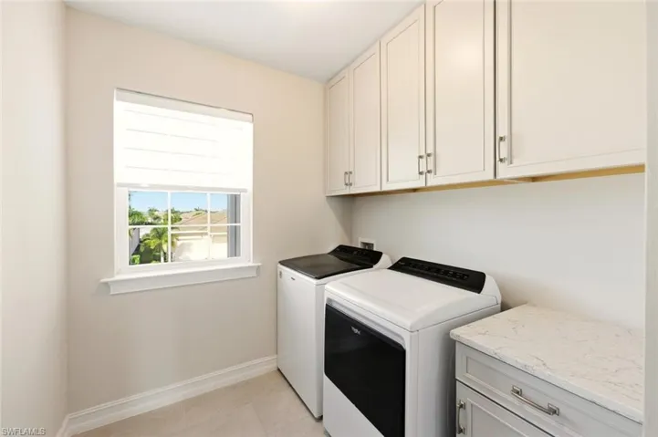 Laundry area with cabinet space, washing machine and dryer, and light tile patterned flooring