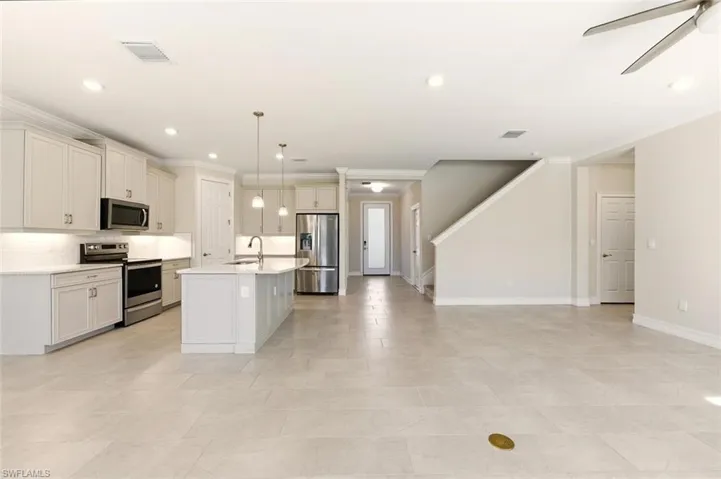 Kitchen featuring stainless steel appliances, a ceiling fan, a center island with sink, open floor plan, and hanging light fixtures