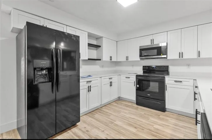 Kitchen with black appliances, white cabinetry, open shelves, and light wood-type flooring