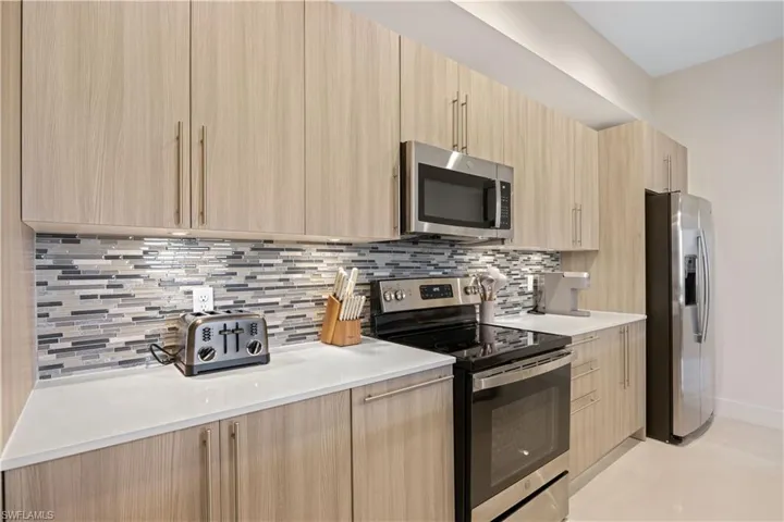 Kitchen featuring backsplash, appliances with stainless steel finishes, light brown cabinets, and modern cabinets