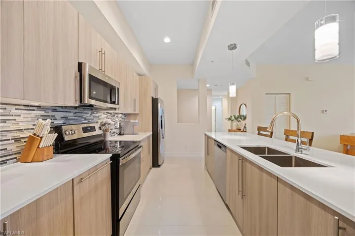 Kitchen with modern cabinets, appliances with stainless steel finishes, a sink, light brown cabinets, and backsplash