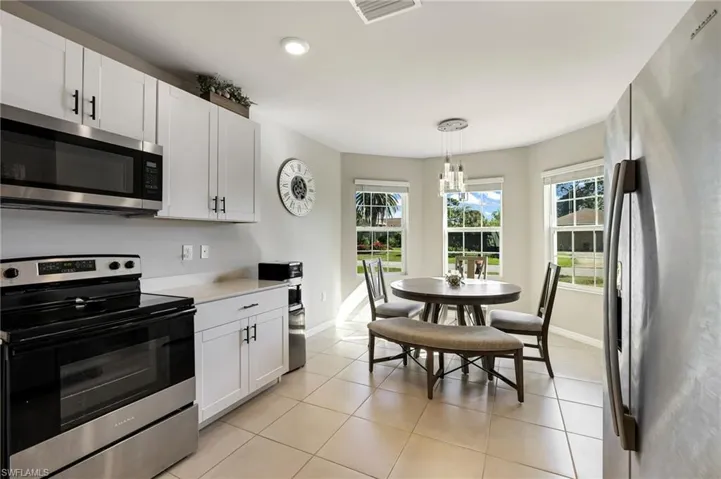 Kitchen with appliances with stainless steel finishes, light tile patterned floors, an inviting chandelier, white cabinets, and hanging light fixtures