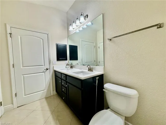 Bathroom with toilet, dual bowl vanity, and tile patterned flooring