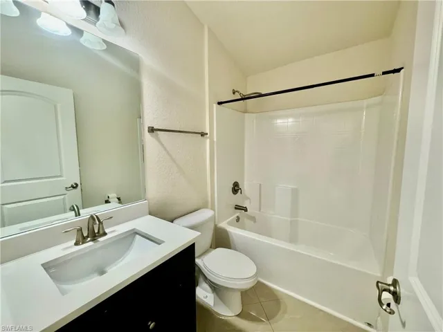 Full bathroom with washtub / shower combination, toilet, tile patterned floors, and vanity