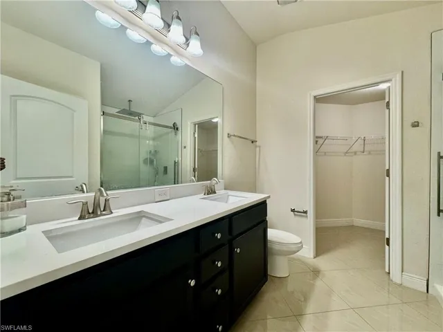 Bathroom with lofted ceiling, toilet, tile patterned floors, dual vanity, and walk in shower