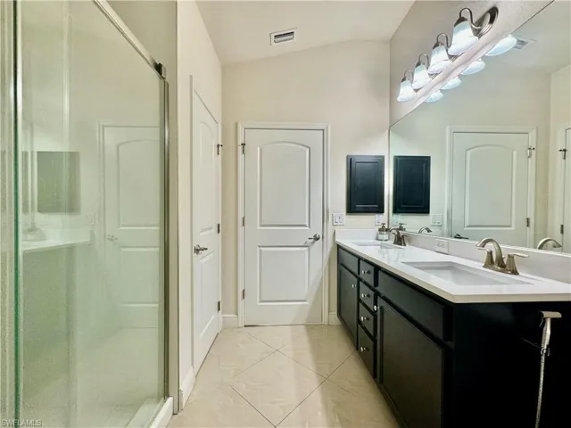 Bathroom featuring lofted ceiling, dual bowl vanity, a shower with shower door, and tile patterned flooring