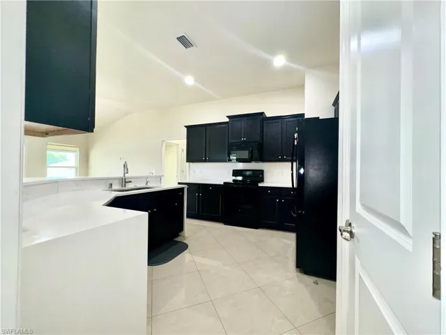 Kitchen featuring light tile patterned floors, lofted ceiling, black appliances, sink, and kitchen peninsula