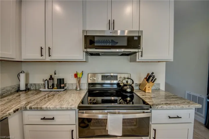 Kitchen featuring appliances with stainless steel finishes, white cabinets, and light stone counters