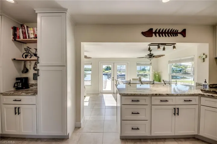 Kitchen with a peninsula, light tile patterned floors, light stone countertops, french doors, and white cabinets