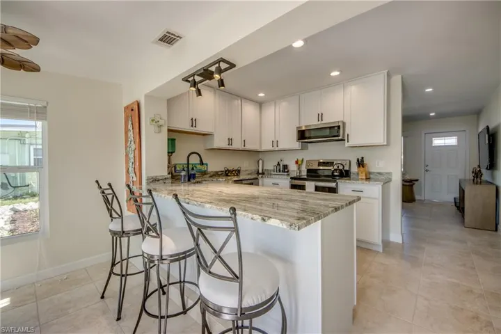 Kitchen featuring stainless steel appliances, light stone countertops, white cabinets, a peninsula, and light tile patterned floors
