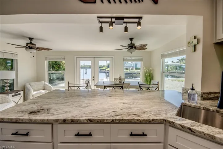 Kitchen with ceiling fan, light stone counters, white cabinets, a water view, and french doors