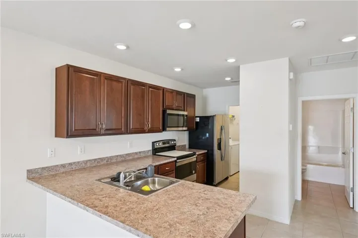 Kitchen with light countertops, stainless steel appliances, dark brown cabinetry, light tile patterned floors, and a peninsula