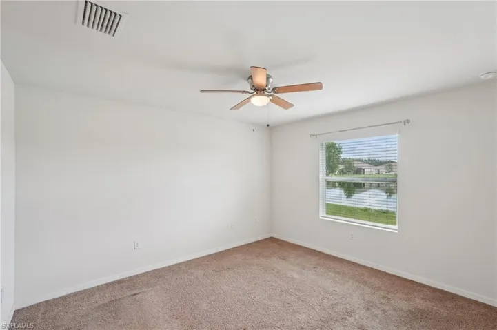 Carpeted spare room featuring a water view and ceiling fan